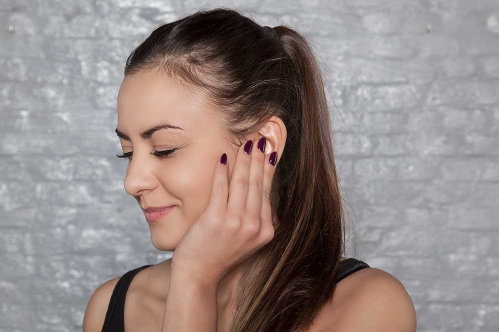 Young woman gently touching her ear over a full, clogged feeling, a concern North Hills Hearing & Balance Center sees in Hurst, TX